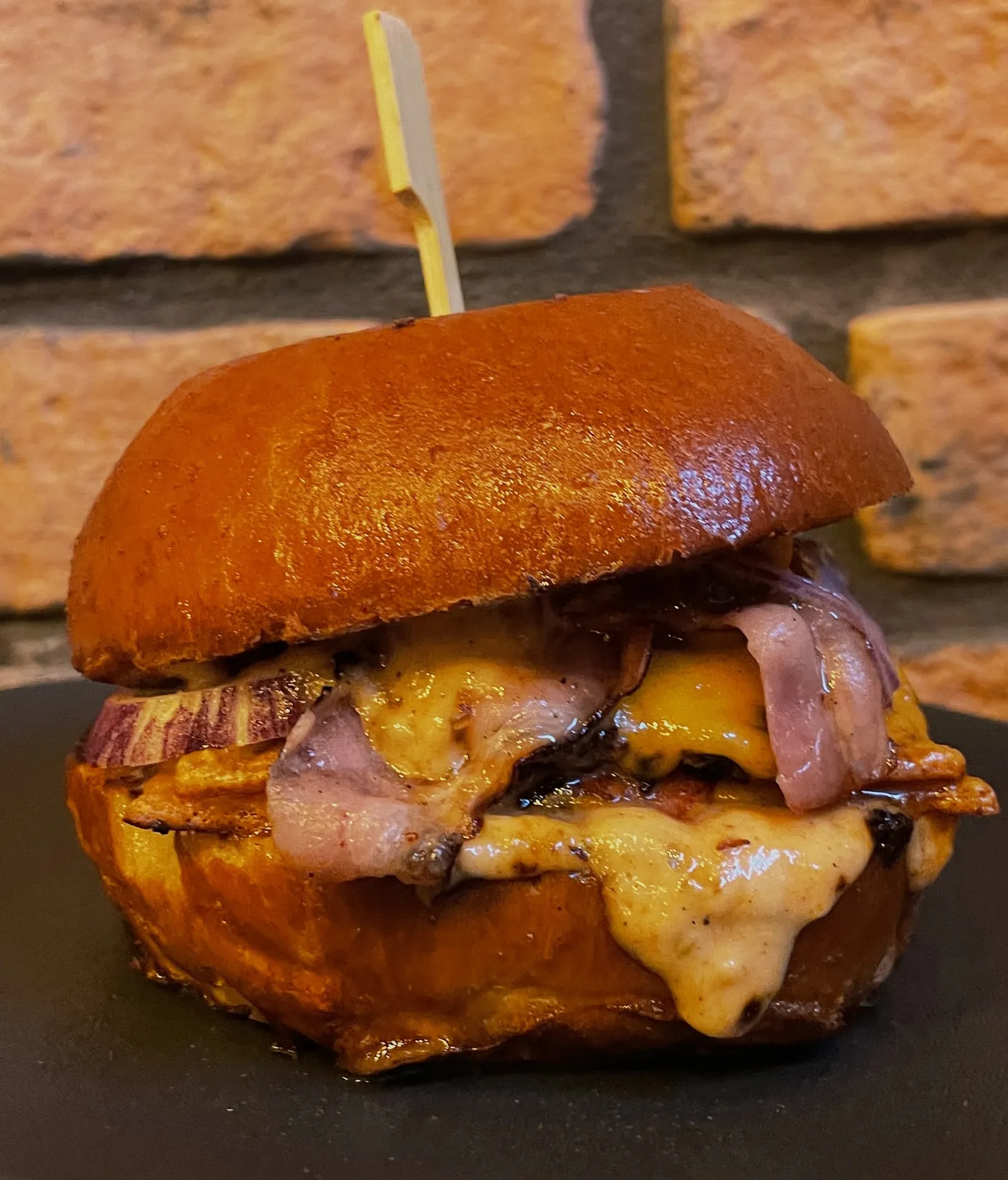 Šťavnatý burger s roztopeným cheddarom a slaninou na pozadí tehlovej steny