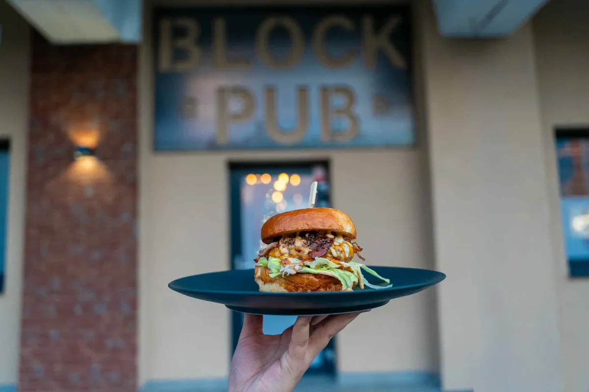 Burger v ruke pred vývesným štítom BLOCK PUB