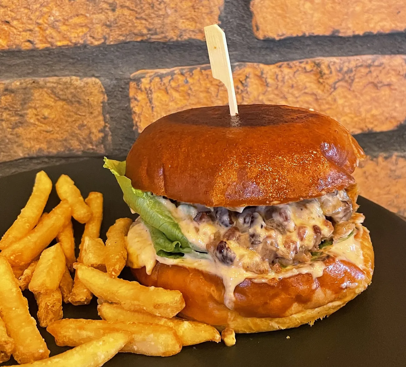 Burger s lesklou domácou žemľou a hranolkami na čiernom tanieri